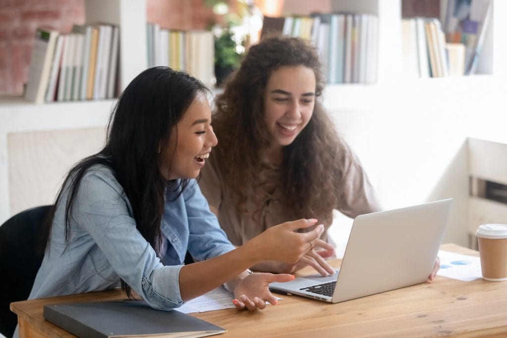 Funny diverse girls laughing watching video online on laptop